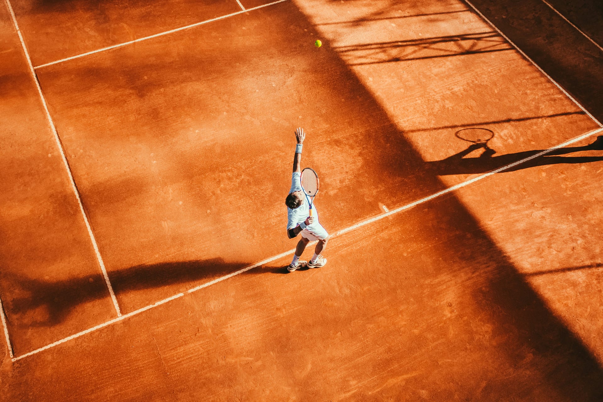 Tennisspieler beim Aufschlag auf einem Sandplatz, von oben fotografiert